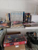 Photo showing collection of 9 VHS tapes, Star Trek Encyclopedia, several TV Guide magazines, and the puzzle box on metal shelving