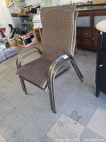 Side angle view of one aluminum frame patio chair showing brown mesh seat and backrest, curved armrest, and slight weathering on metal frame.