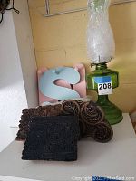 Green glass hurricane lamp displayed with additional chimney wrapped in bubble wrap and alongside wooden print blocks.