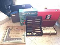 Wide view showing the collection of games including Trivial Pursuit, Scattergories, Voltaire, backgammon set open showing pieces, dominoes set, and black storage box.