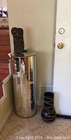 Mirrored cylindrical pedestal and black floor vase side by side against wall near stairs.