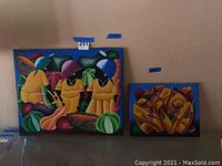 Overview of both unframed canvas paintings side by side leaning against wall