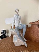 Front-left side view of the Lladro figurine showing boy seated on rock reading book.