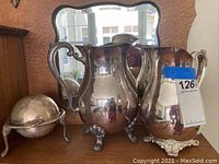 Photo showing two silver plate pitchers and the vintage roll top butter dish together on a surface with a mirror behind.