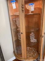 View of wooden display cabinet with glass shelves showing multiple crystal items including bowls, decanter, platter, and ashtray.