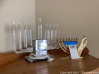 Photo showing both menorahs: electric glass menorah on the left and brass menorah on the right with price tag.