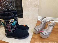 Pair of black Ugg embroidered boots standing next to silver Steve Madden platform heels on floor