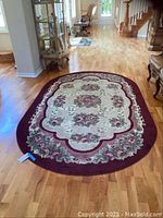 Photo of oval floral area rug with burgundy border and cream center on hardwood floor