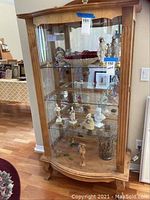 Full view of wooden china cabinet containing porcelain figurines, glass vases, and decorative items on four glass shelves.