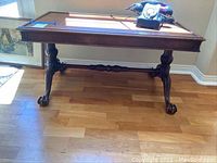 Front side view of wooden table showing claw feet and carved stretcher bar between legs on wooden floor.