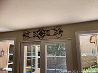 Scrolled metal wall art mounted above sliding door, showing full width and placement in room.
