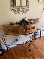 Half round wood and iron occasional table with rounded wood top and single drawer. Decorative iron legs curved in scrollwork. Table positioned against wall with various items on top.