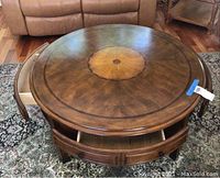 Front-facing view of round wood coffee table showing inlay and two drawers slightly open on opposite sides.
