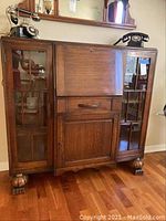 Front view of vintage wood secretary desk cabinet showing drop down writing surface and glass paneled side doors.