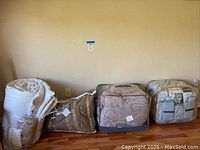 Four king size comforters in different packaging and colors, positioned against a wall on a wooden floor.