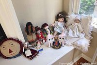 Wide view of assortment including dolls, cat bookends, and rag doll pillow on windowsill