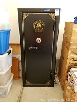 Front view of closed safe showing black door, gold logo and decoration, handle and lock
