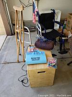Shows wheelchair, walker, wooden crutches, storage cabinet, Titan Fitness step box with items on top including a massage heat pillow, pedometer and a pack of small accessories.