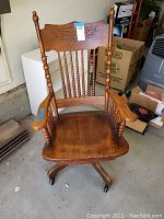 Front view of antique wooden swivel rocker chair showing turned wood detailing, carved floral back panel, and spindle backrest.