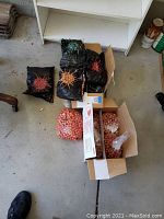 Overview of multiple bags and boxes containing paint balls in orange and red colors, some bags show damage or spillage.