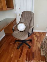 Beige office chair with wall clock placed on seat on wood floor near built-in desk.