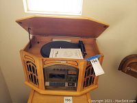 Side view of wooden entertainment cabinet with phonograph turntable under hinged lid and decorative speaker panels.