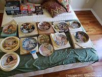 Wide view of 13 collector plates with children and family scenes, some boxed, laid on a bed