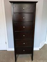Front view of tall dark wood lingerie cabinet with six drawers and metal knobs.