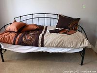 Full view of the black metal daybed with bedding including comforter, pillows, and mattress, showing the curved metal frame