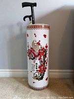 Full view of white porcelain umbrella/cane stand with red crane and floral design holding two black canes.