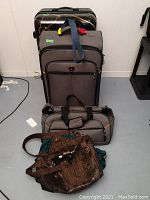 Photo showing hard sided black suitcase and two soft sided suitcases stacked by the wall.