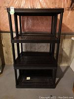 Full view of stacked black plastic shelf unit with four shelves visible, showing perforated shelf surfaces and black posts.