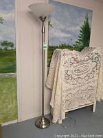 Full view of the tall metal floor lamp with frosted glass shade against a wall and draped furniture.