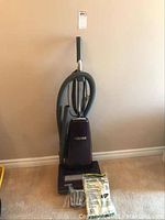 Front view of dark purple Kenmore upright vacuum cleaner with handle and extra vacuum bags and belt at the base.