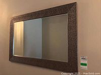 Front view of rectangular wall mirror with textured dark metallic frame hung on beige wall.