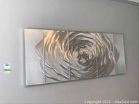 Five separate aluminum wall panels arranged together on a gray wall, forming a continuous silver rose design across the panels.
