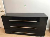 Front view of glossy black three drawer dresser with silver handles
