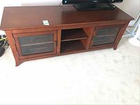 Full view of solid wood TV stand with glass front doors and flat top surface holding a TV.