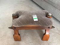 Front view of the wooden camel saddle stool showing padded seat and wooden legs with metal finials.