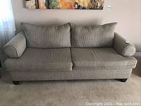 Front view of the beige fabric covered sofa showing two seat cushions, two back cushions with removable covers, rolled arms and dark wooden legs.