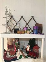 Wire Christmas trees, wooden expandable coat hanger, ribbons, small boxes, figurines including two nutcrackers, Santa, small artificial Christmas tree, clear wine glass, and red lantern on shelving unit