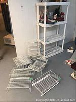 Full image of assorted white wire racks and white four tier plastic shelving unit containing holiday figurines on top shelves.