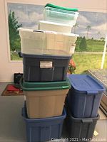 Stack of seven storage totes in various sizes and colors including blue, beige, and clear with corresponding lids.
