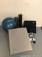 Photo showing large blue Tempo Fitness exercise ball, beige large wedge pillow, two rolled exercise mats, medium black wedge pillow, handheld massager, Tens machine and accessories arranged on floor.