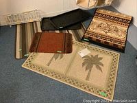 Photo showing four mats stacked and spread partially on the floor, including a palm tree patterned mat, a brown floral patterned mat, a large striped mat, and an orange patterned mat, along with two black plastic boot trays and a white plastic shoe rack.