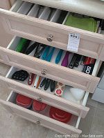 Four opened drawers showing assorted kitchen flatware, cutlery, knives, tools, food storage containers, and kitchen cloths.