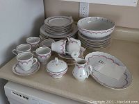 Full view of the dinnerware set arranged on a counter, showing stacked plates, teacups, saucers, and serving pieces including sugar bowl and creamer.