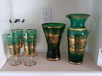 Wide photo showing the green glass pitcher, vase, four matching stemmed glasses, and the four music-themed swizzle sticks on display.