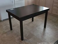 Dining table shown from a corner angle, highlighting the rectangular top and sturdy legs on a light tile floor.