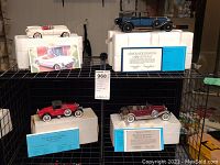 Overview of four Franklin Mint 1:24 scale model cars displayed on metal shelves with original boxes and certificates of authenticity.